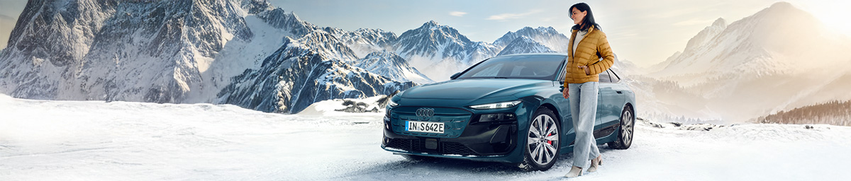 Ein blauer Elektro-SUV fährt durch Schneematsch vor einer modernen Garage mit Ladestation.