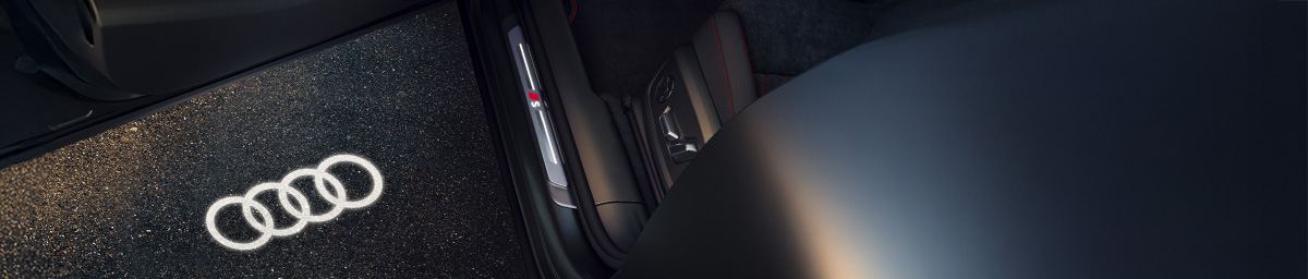 Innenansicht einer geöffneten Autotür mit beleuchtetem Audi-Logo auf dem Boden.